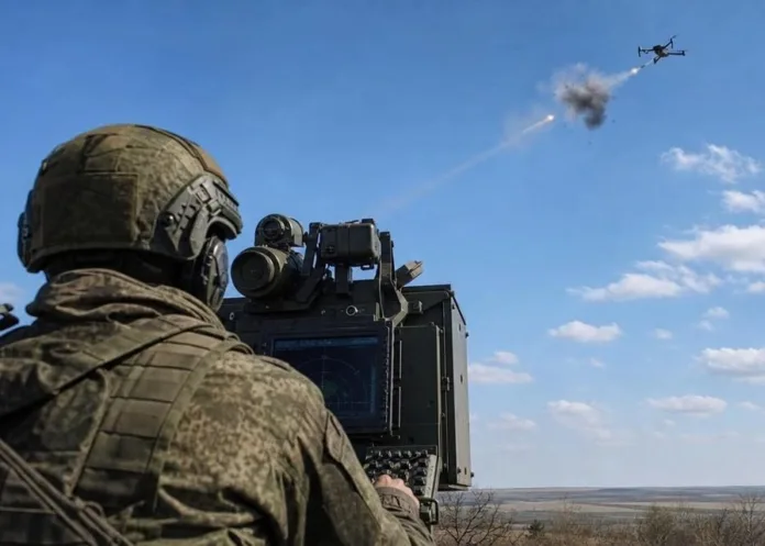 Военный в камуфляже работает у радиолокационного оборудования, наблюдая за вертолётом и облаком дыма в небе.