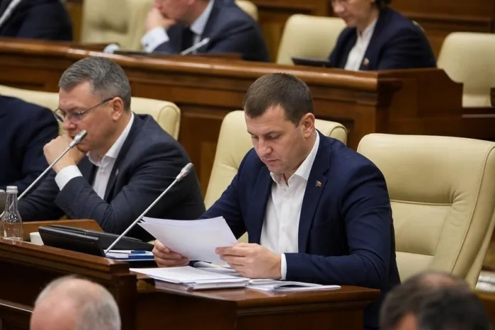 Мужчина в деловом костюме читает бумаги за столом в зале заседаний; рядом сидят другие участники.
