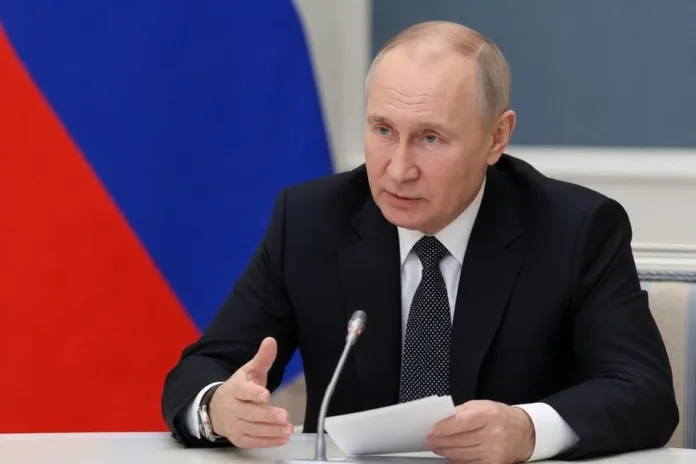 Владимир Путин сидит за столом с документом перед микрофоном; на заднем плане виден российский флаг.