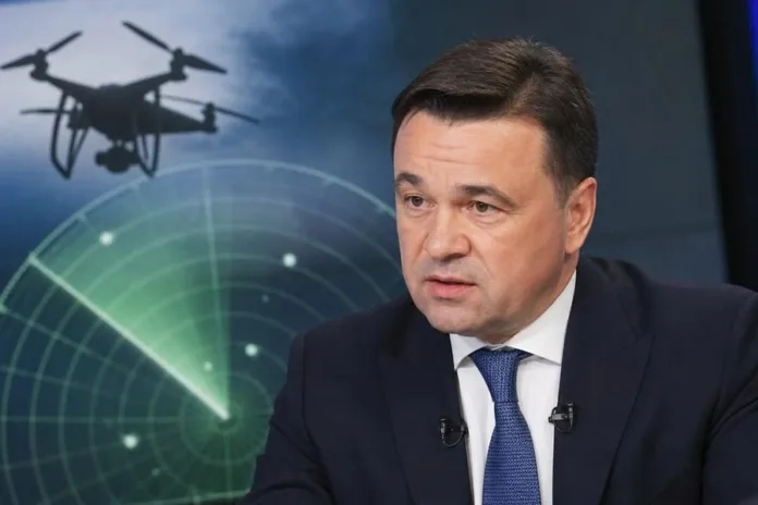 Мужчина в деловом костюме сидит на фоне изображения дрона и радиолокационного экрана.