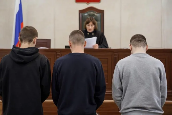 В зале суда женщина-судья читает документ перед тремя мужчинами, стоящими спиной к камере.