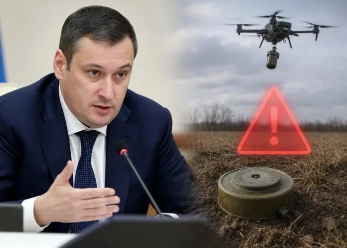 Мужчина в деловом костюме выступает у микрофона; рядом показаны дрон над полем, предупреждающий знак и предмет, похожий на мину.