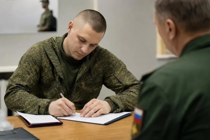 Военнослужащий в камуфляжной форме сидит за столом и пишет в документе напротив другого человека в форме.